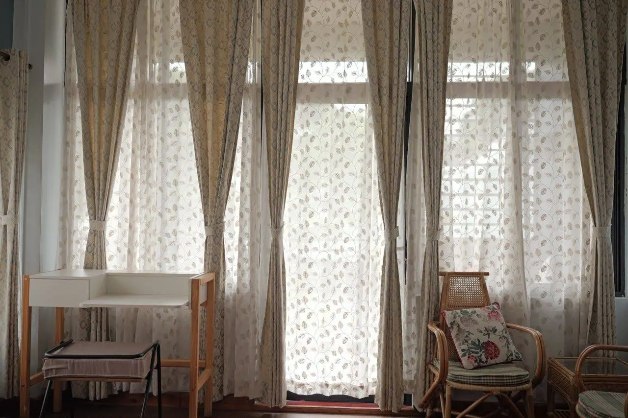 A cane armchair and writing desk beside sheer curtains in soft afternoon light