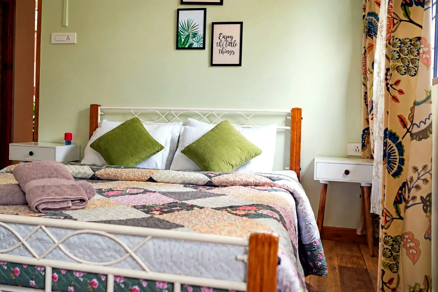 Areca room with sage green walls, botanical prints and a white iron bed with wooden posts